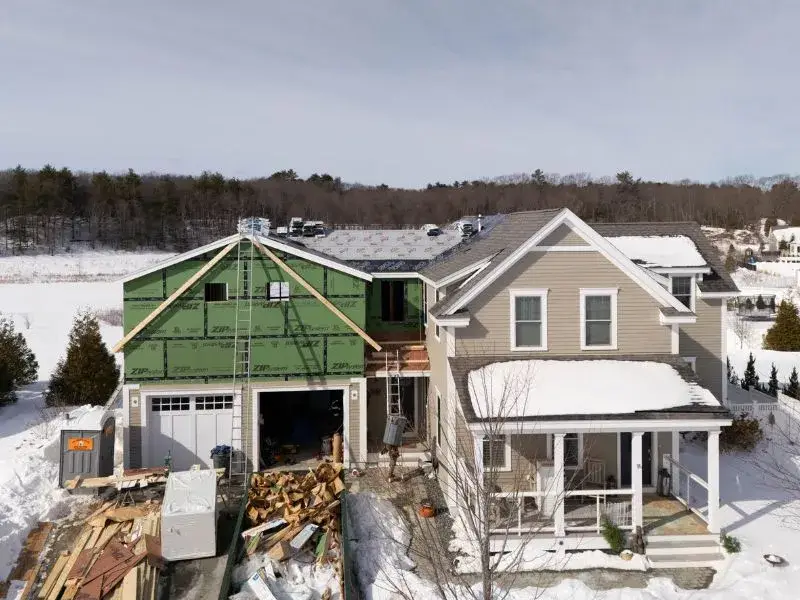 Aerial view of a residential construction site showing a garage conversion into an Accessory Dwelling Unit (ADU) with green framing, snow-covered surroundings, and construction materials, relevant to Massachusetts homeowners exploring garage-to-ADU transformations.