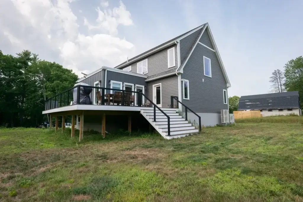 Modern gray house with a deck, surrounded by grass and trees.