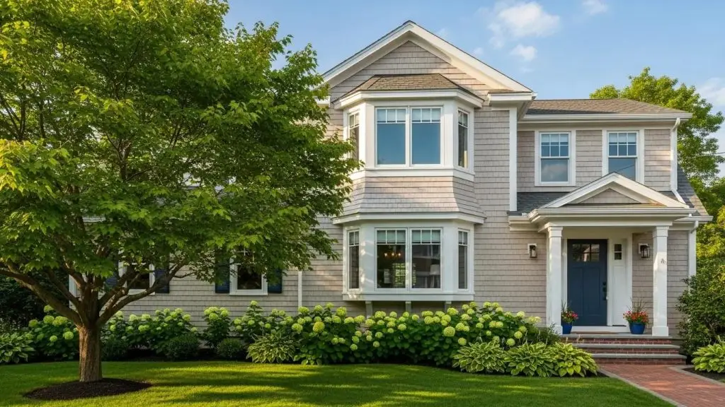 North Shore MA home featuring a second-story addition, landscaped front yard with greenery and flowering plants, sunny outdoor setting.