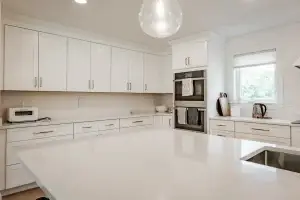 Modern kitchen with white cabinetry, quartz island, and stainless steel appliances.