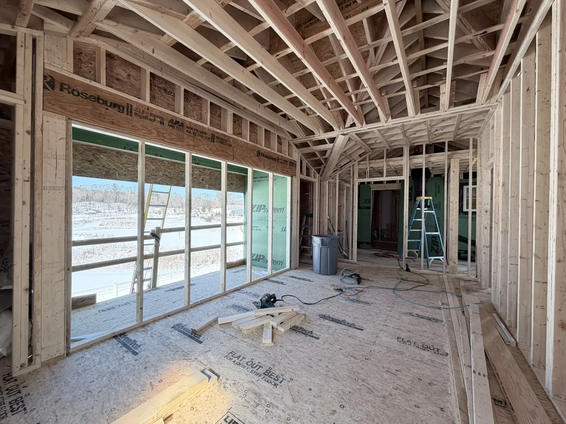 Unfinished primary suite showing roof framing and the balcony window wall