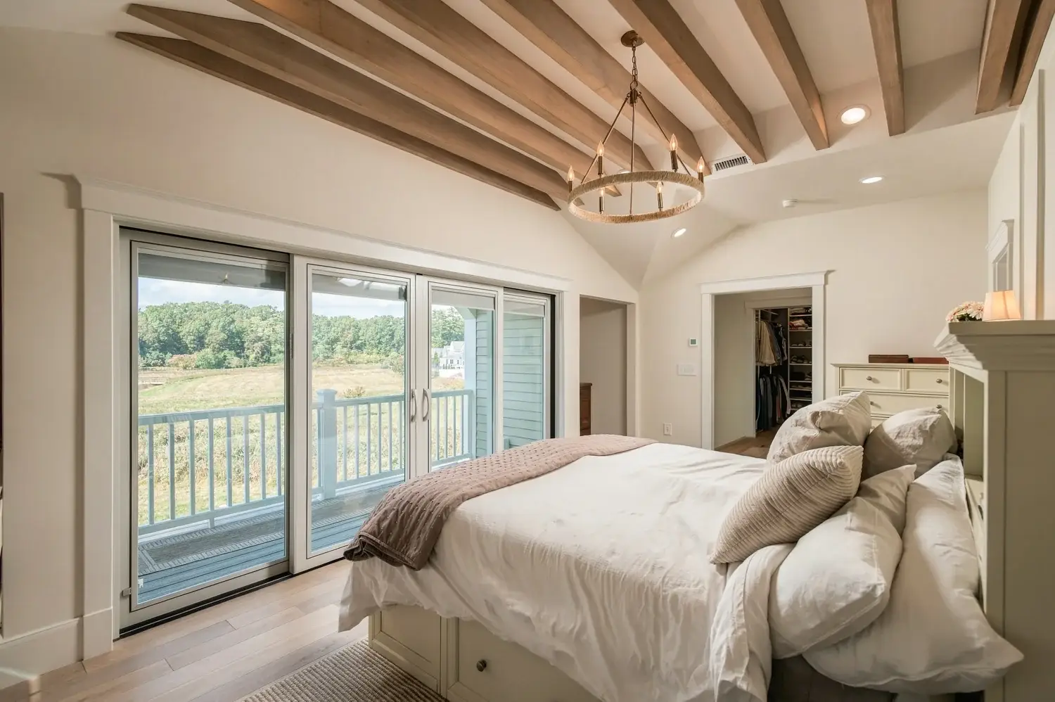 Completed primary bedroom with exposed wood beams and sliding doors to the balcony