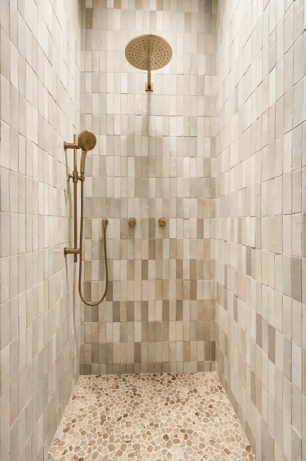 Brass rainfall shower and body sprays against vertically laid pale tile